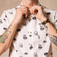White button up shirt with tortoise buttons. Patterned with skulls, donuts, coffee and eyes. 