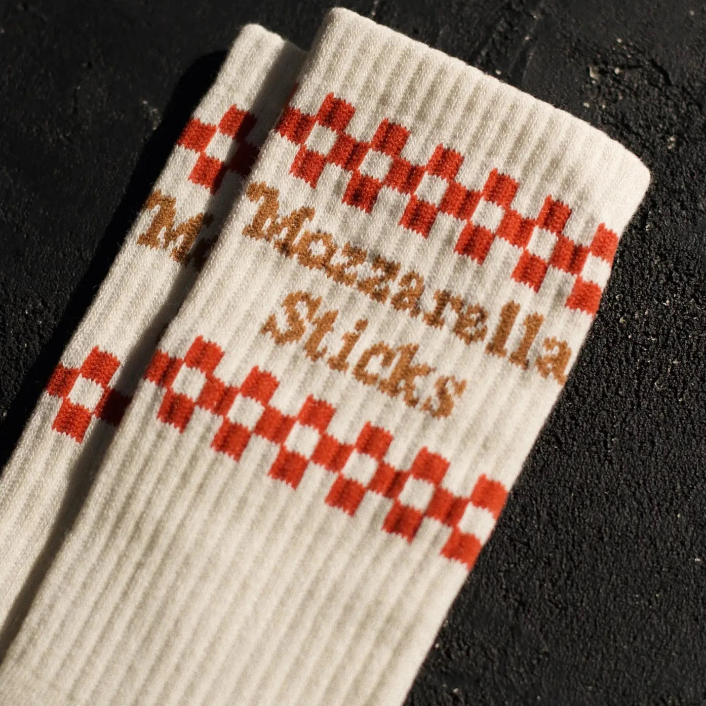 Cream colored socks with red checkerboard. Brown text that reads Mozzarella Sticks