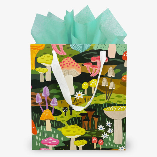 Gift bag featuring a mutitude of mushrooms in several different colors. Bag has white rope handles and teal tissue paper.