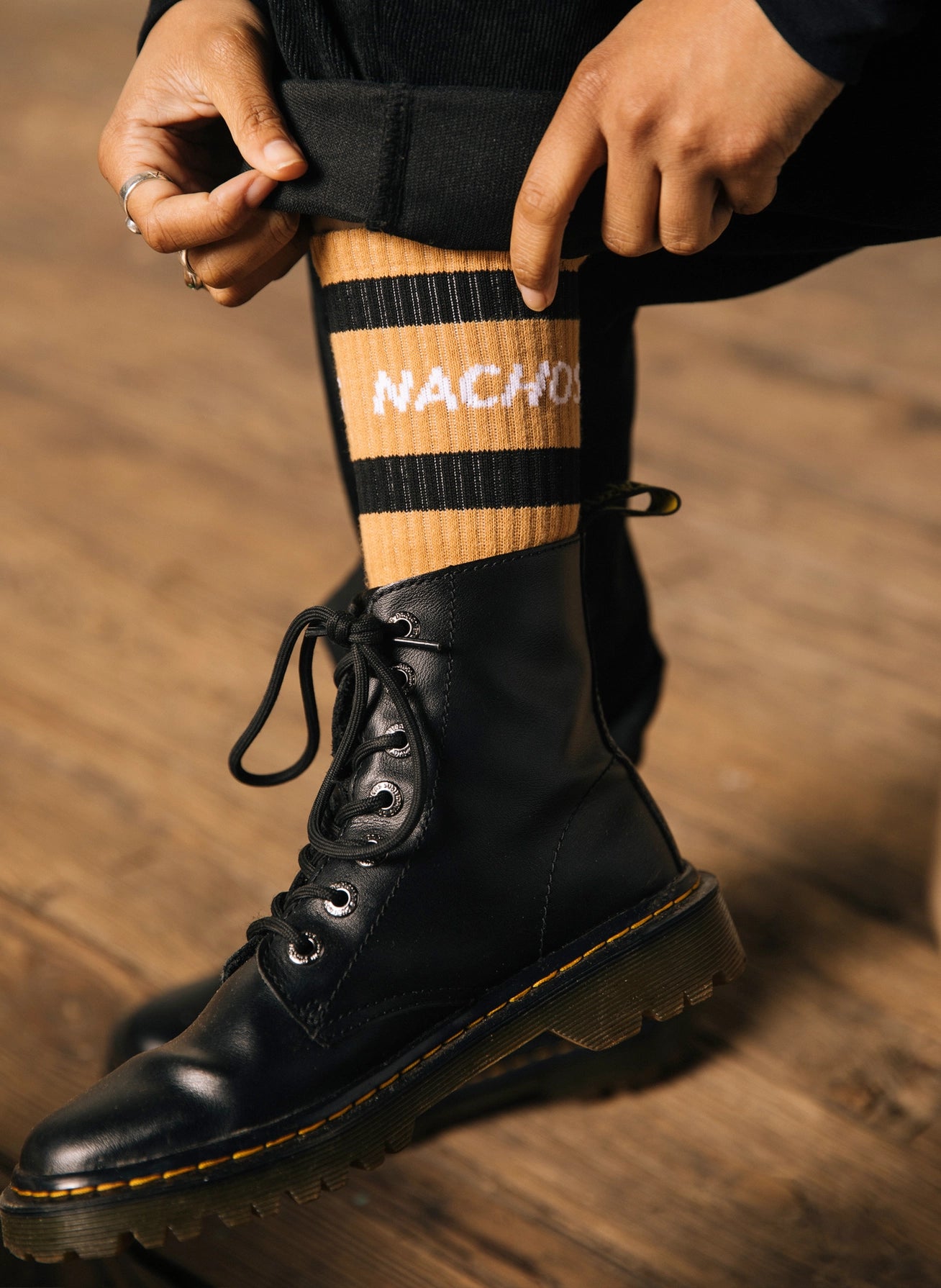 Nachos socks. Model is wearing Doc Martin Boots and high black pants to show off the sock's stripes and words.