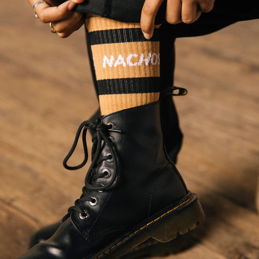 Nachos socks. Model is wearing Doc Martin Boots and high black pants to show off the sock's stripes and words.