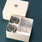 Set of colorful sake glass set in a box with a visible brand logo on a dark blue background.