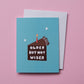 A light blue birthday card with a cartoon cake illustration and the text 'OLDER BUT NOT WISER' in white, shown with a white envelope on a solid pink background.