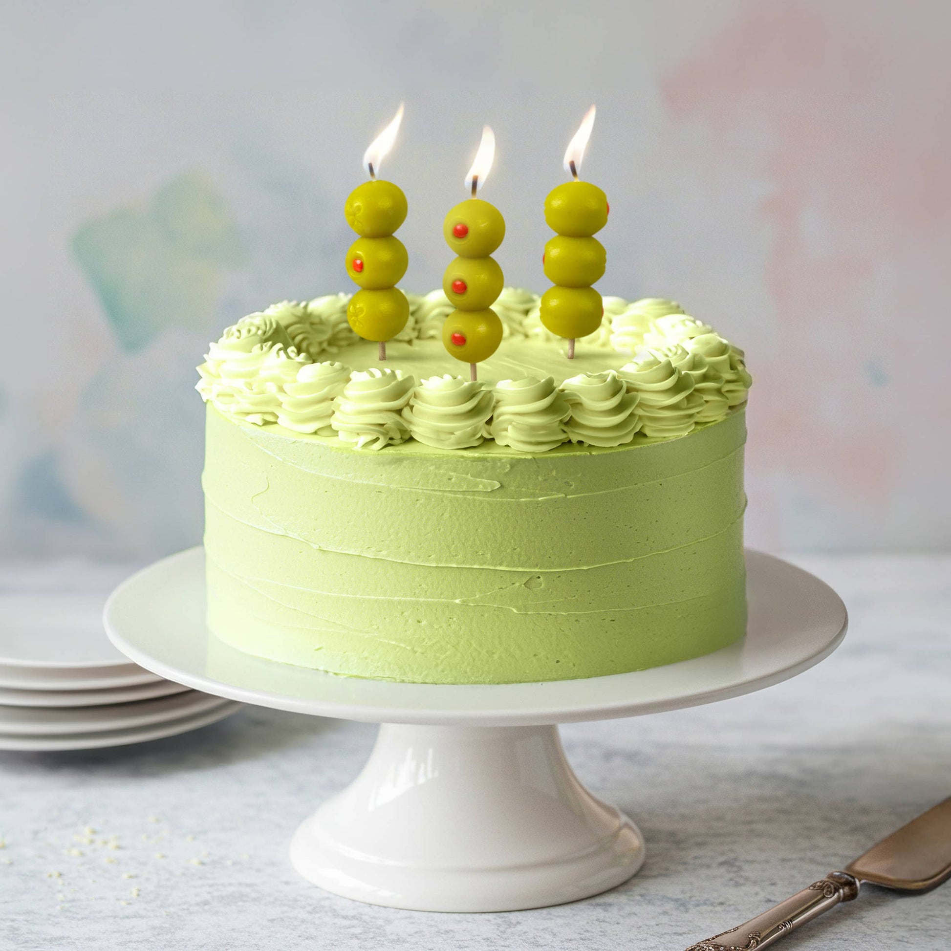 Green cake with candles on a white stand against a light background