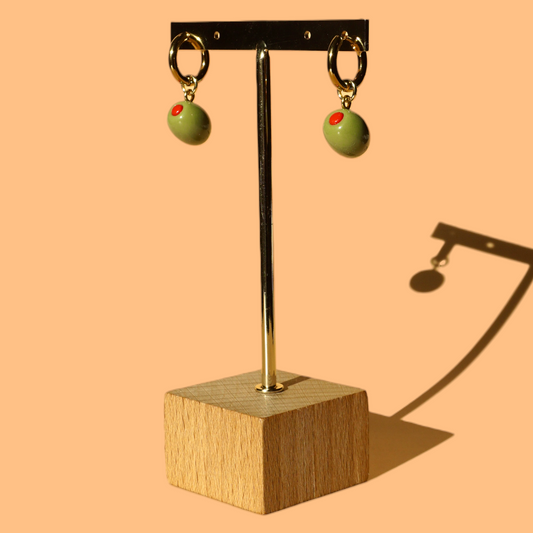 Green Olive earrings on a gold stand with a wooden base against a peach background