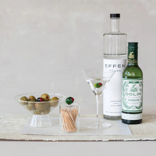 Bottles of vodka and vermouth with a martini glass and olives on a neutral background