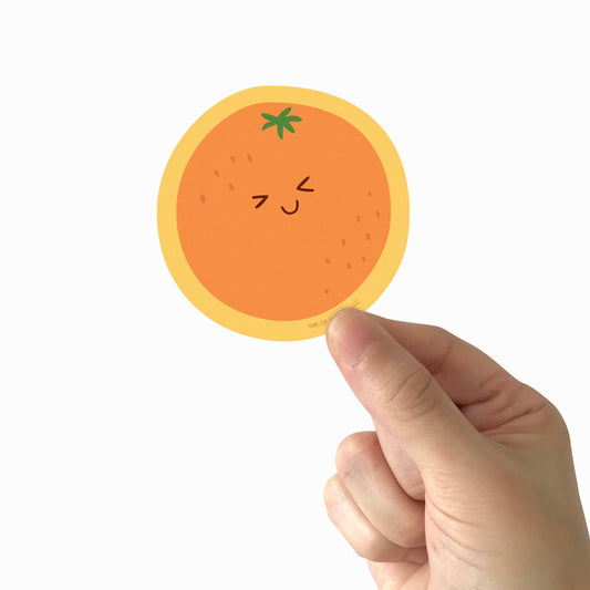 Vinyl sticker of an orange making a cute, smiley face, being held in someone's hand 