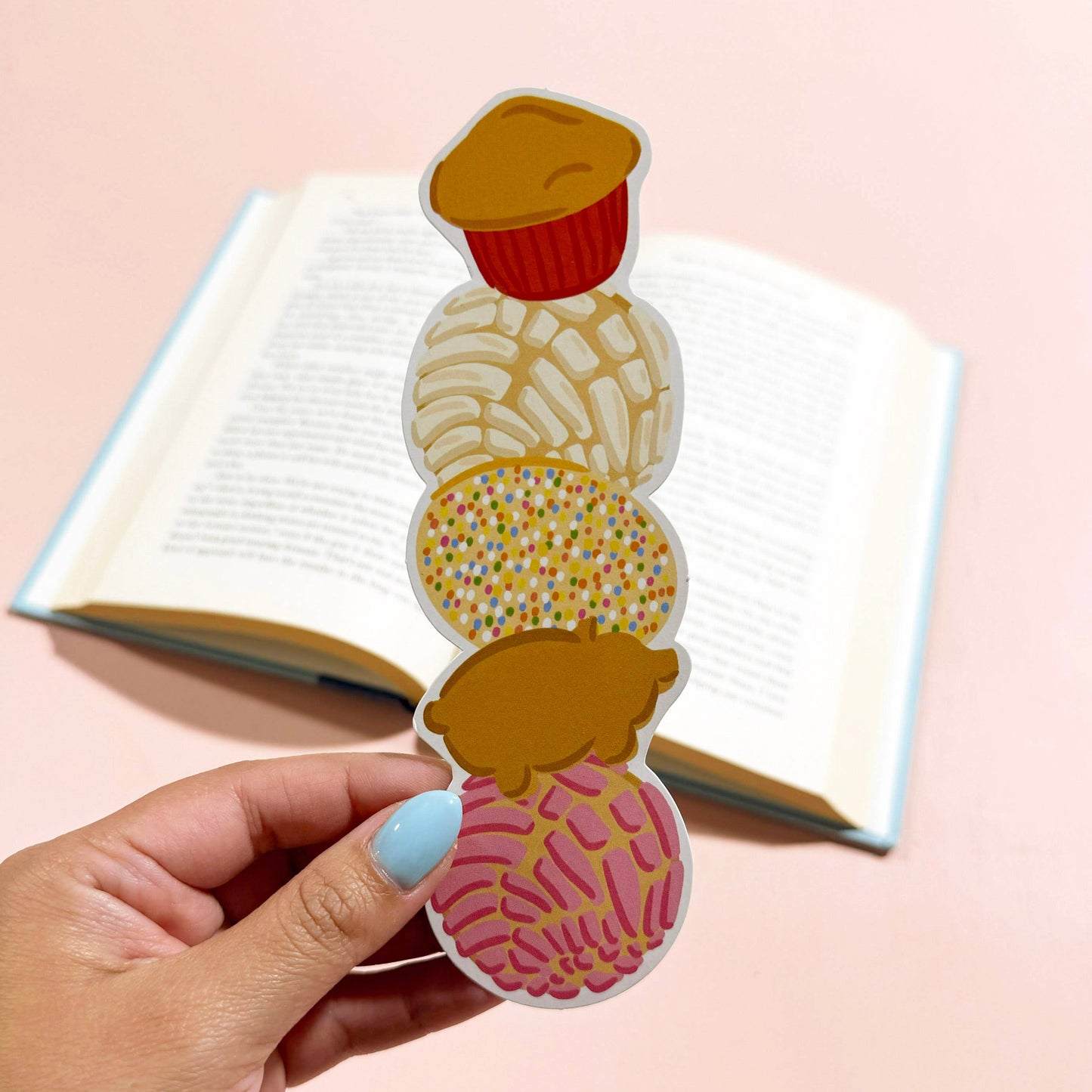 Colorful sweet mexican pastries bookmark held by a hand with a pink background