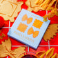 Pasta-shaped napkins on a red checkered tablecloth with pasta pieces around.