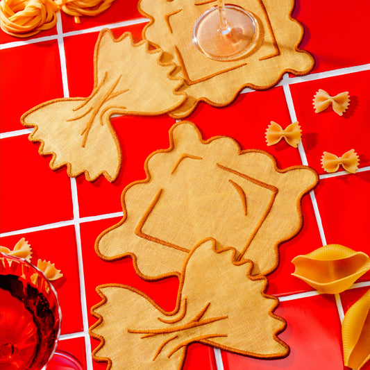 Linen pasta-shaped coasters on a red tiled surface with glasses of red wine.
