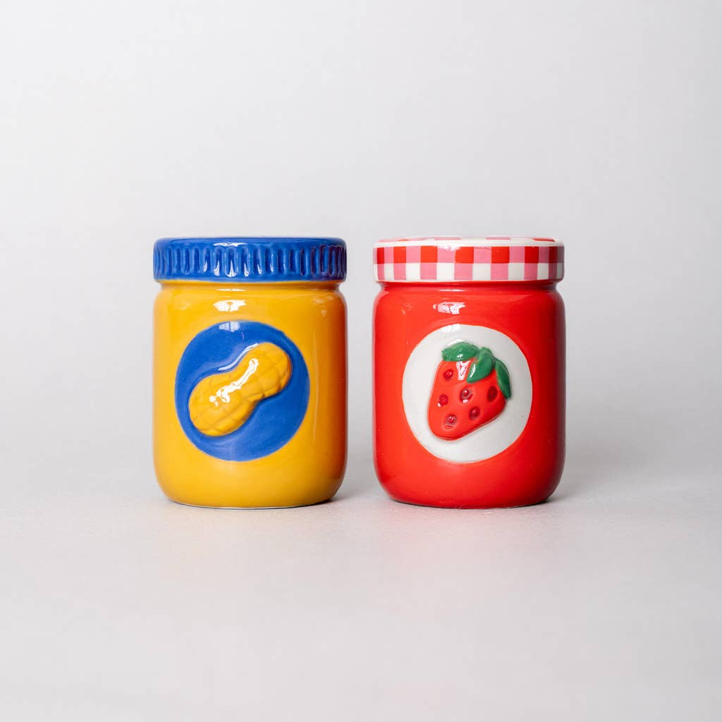 Two colorful jars, one yellow with a blue lid and one red with a white lid, on a light gray background.