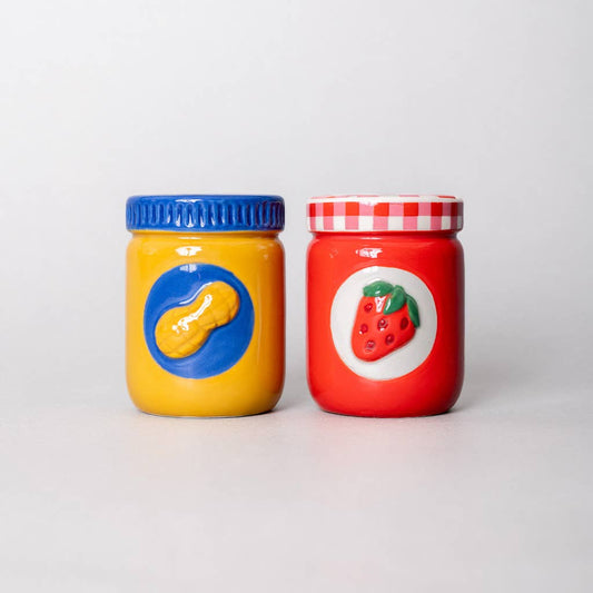 Two colorful jars, one yellow with a blue lid and one red with a white lid, on a light gray background.