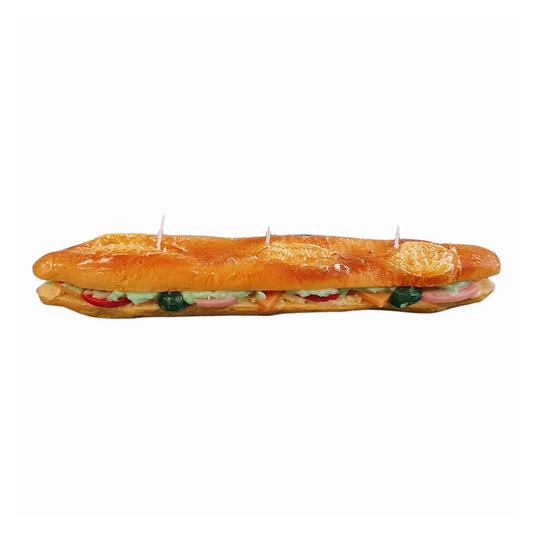 Wax candle shaped like a whole baguette sliced lengthwise and made into a hearty sandwich with many fillings. View from the side.