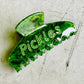 Green sparkly hair clip with "Pickles" written in rhinestones.