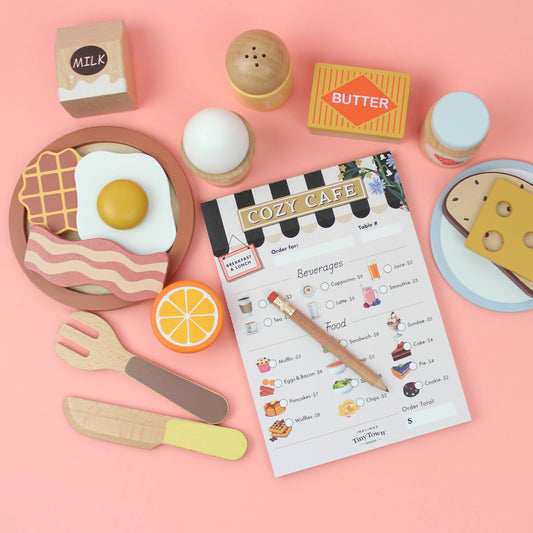 Playful kitchen set with a pretend play menu, utensils, and food items on a pink background