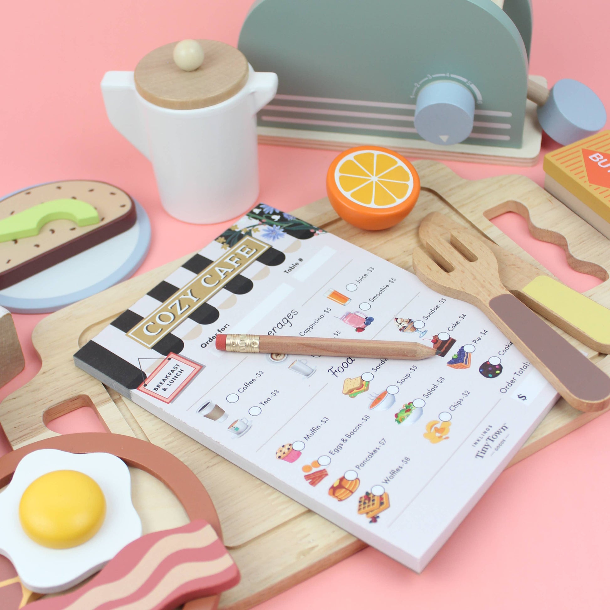 Children's toy kitchen set with a notepad and pen on a pink background