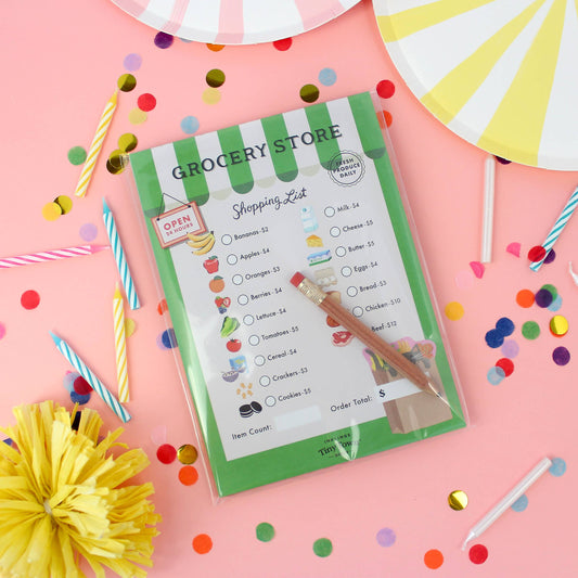 grocery store themed play activity notepad for kids on a pink background with confetti and candles around it 