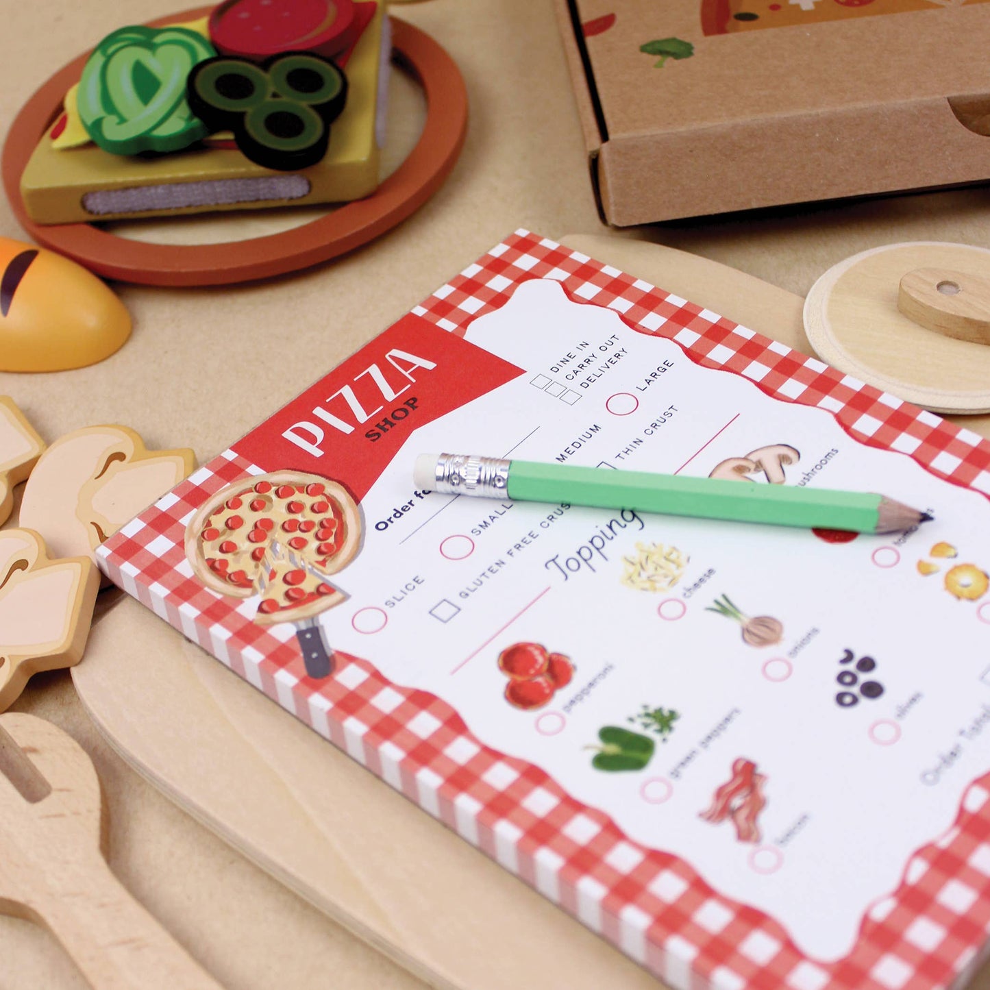 Children's playset with a pizza ordering sheet, toy pizza, and wooden utensils on a table.