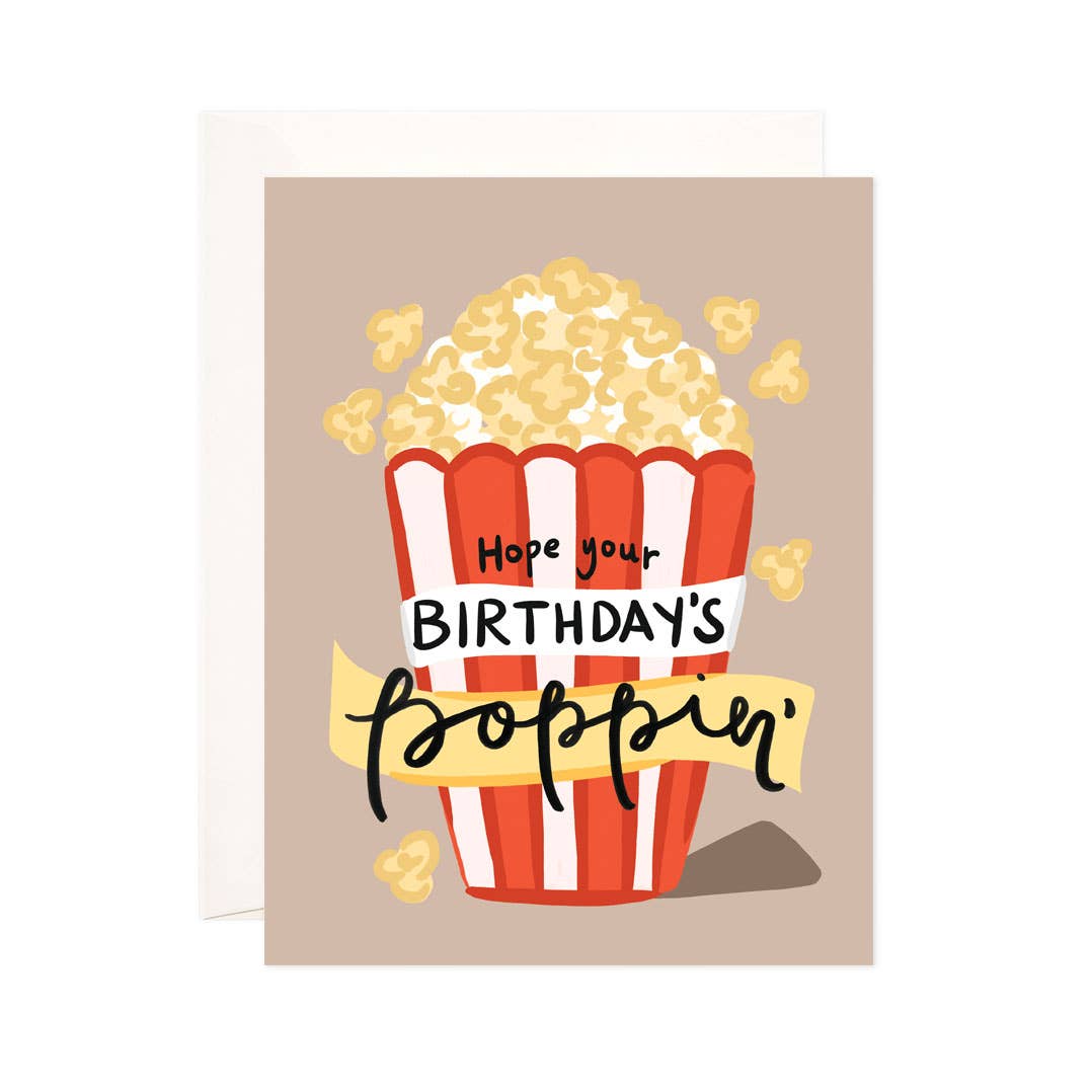 A birthday card featuring a cartoon popcorn bucket with the text 'Hope your BIRTHDAY'S poppin'' on a beige background, shown with a white envelope behind it.