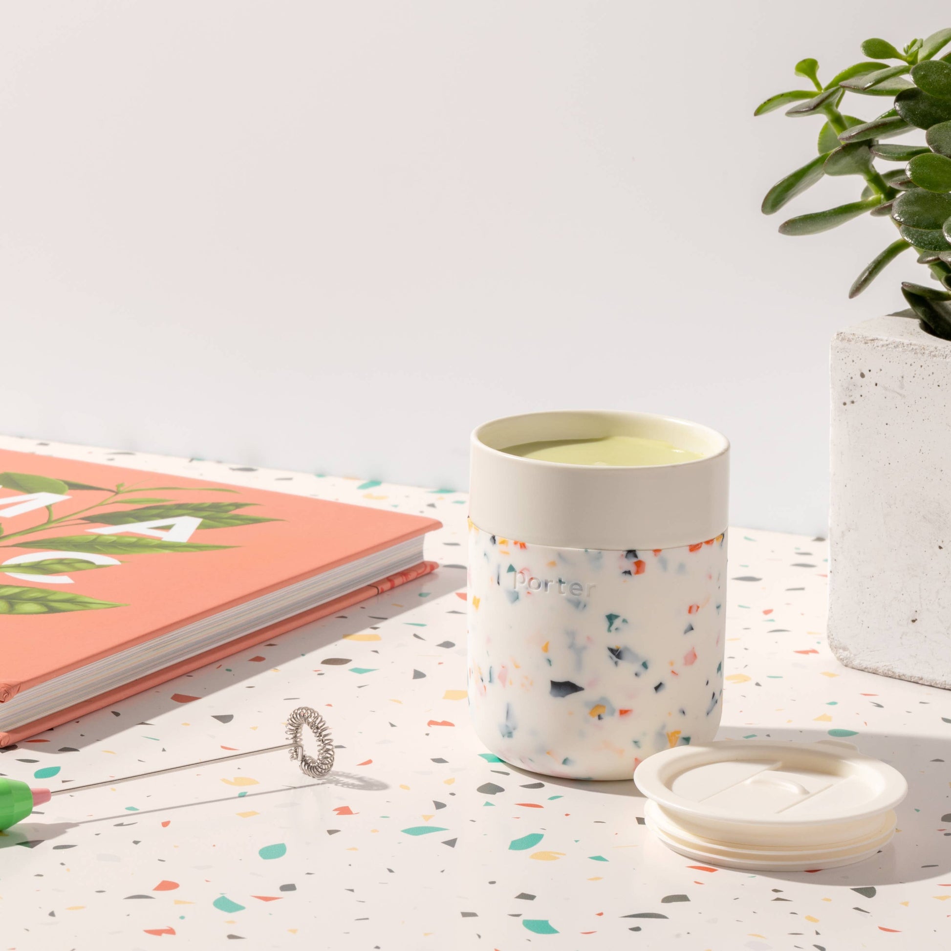 Terrazzo white ceramic mug on a terrazzo table top staged with a book and plant.