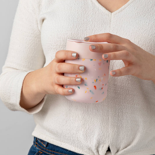 Lady with a white shirt and blue jeans holding a pink terrazzo mug. Model has silver glittery nails.