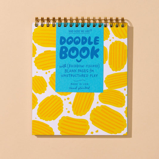 A spiral-bound Doodle Book with a bright blue cover label and a white cover decorated with yellow wavy chip shapes, shown on a warm beige background.