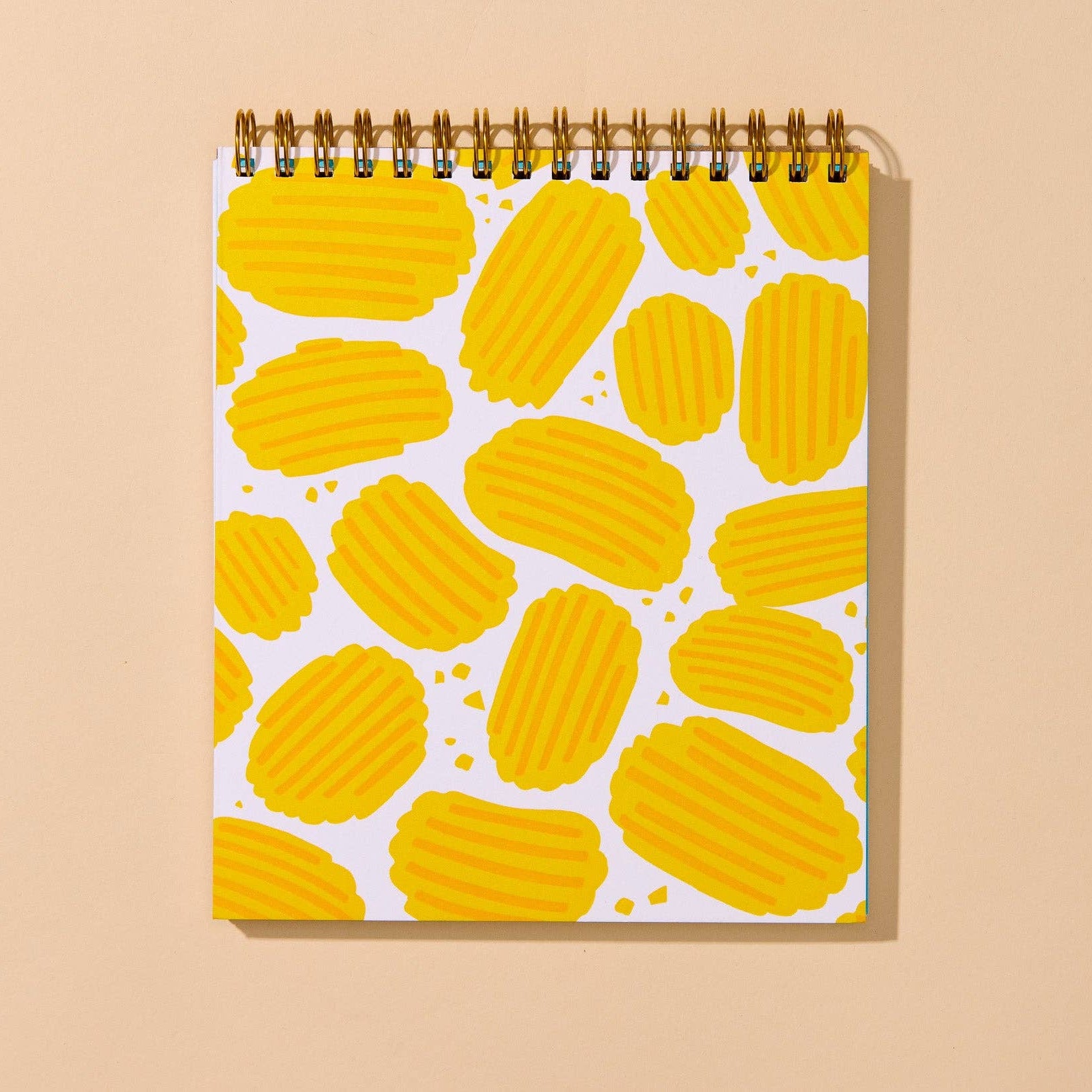 A spiral-bound notebook with a white cover decorated with a pattern of yellow potato chips, displayed against a solid beige background.