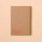 Brown notebook with gold spiral binding on a beige background