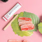 Erasers that look like slices of raw meat on green leaf-shaped memo note with a pencil and tube on a pink background