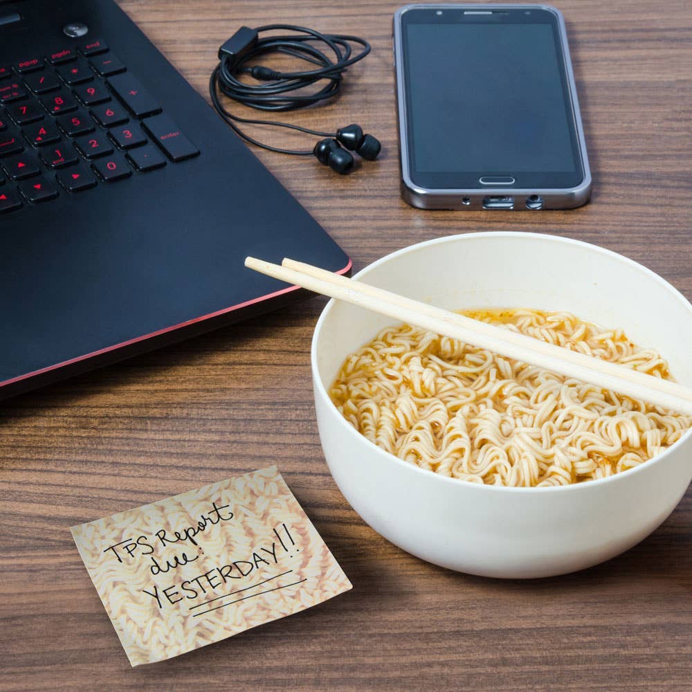 staged photograph with a bowl of real ramen and chopsticks alongside a sticky note pad of paper that looks like a ramen block. 