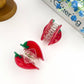 Two red strawberry-shaped hair rollers on a white surface with a magazine in the background.