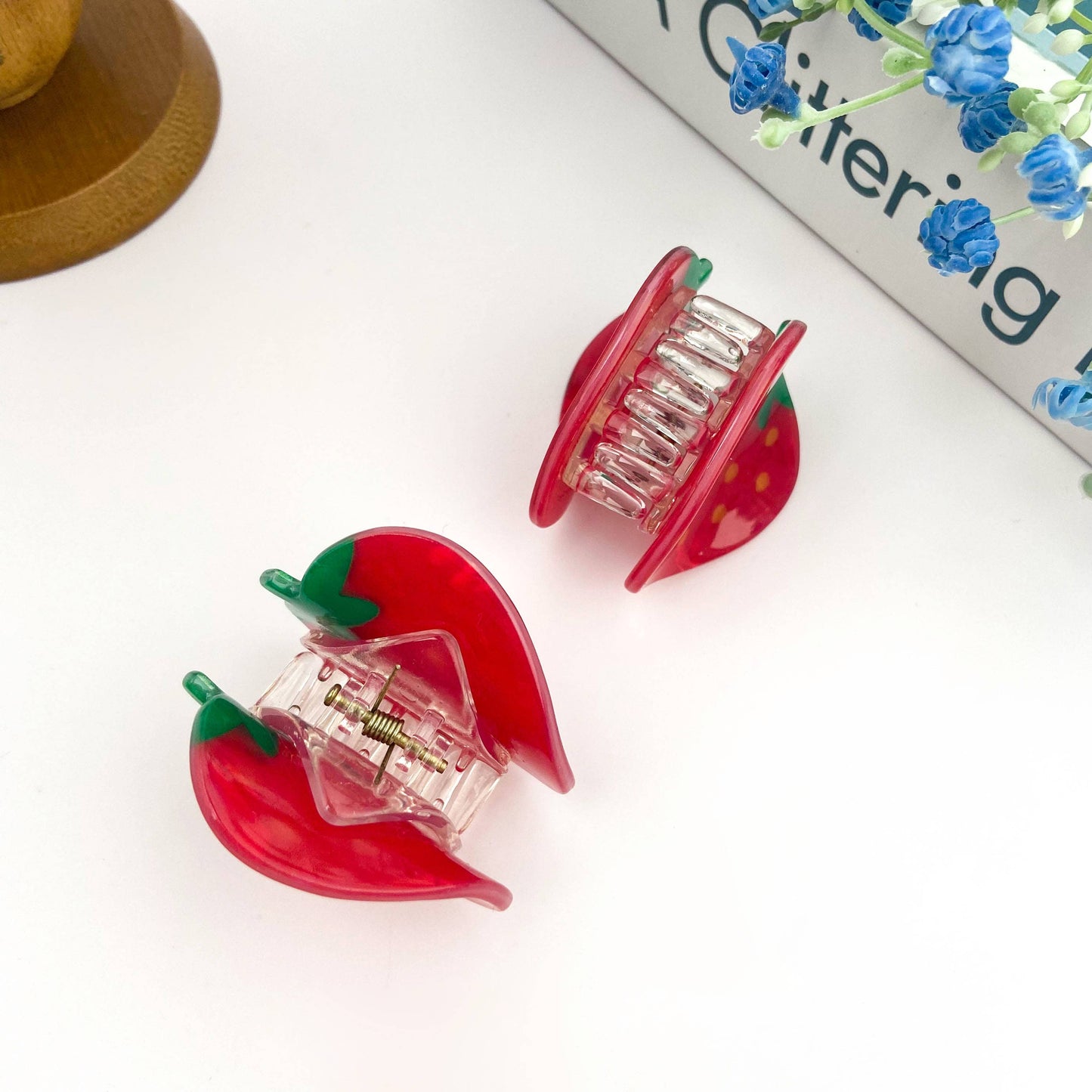 Two red strawberry-shaped hair rollers on a white surface with a magazine in the background.