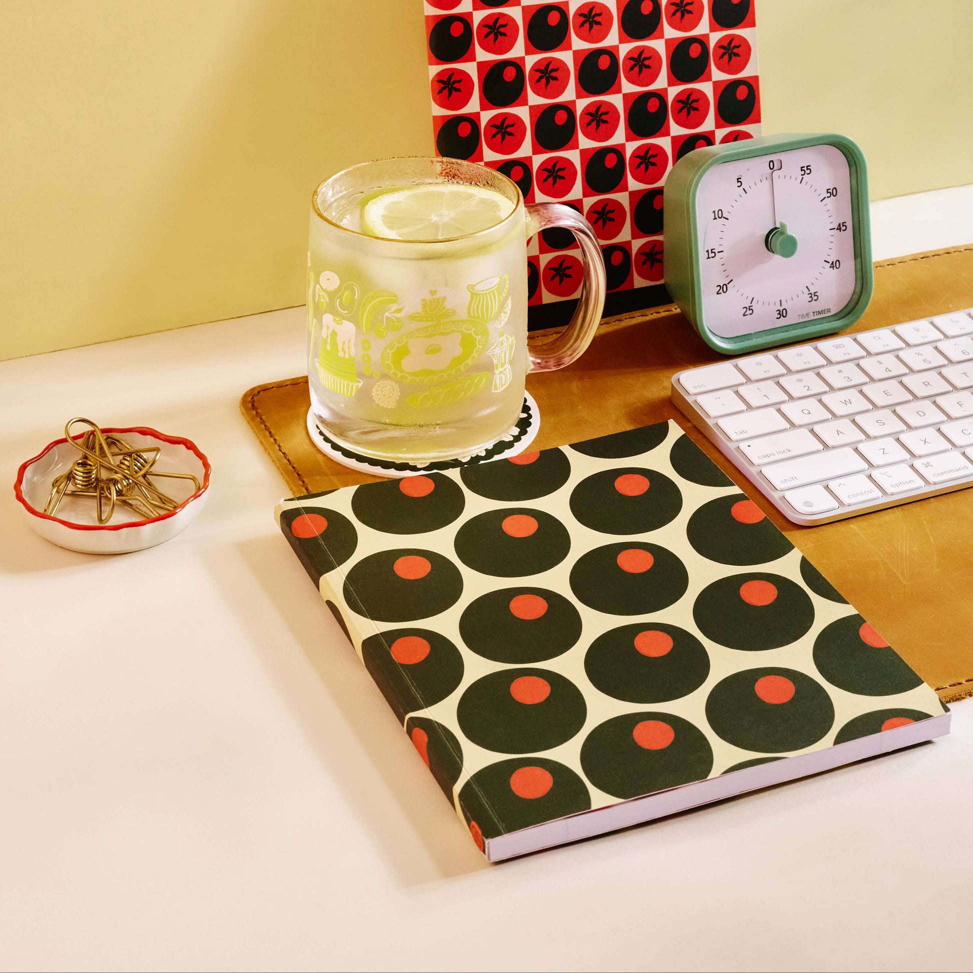 Notebooks with red and black circular patterns on a desk with a glass of water and clock.