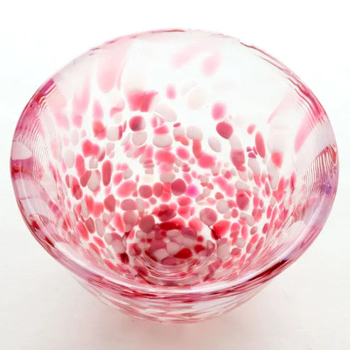 Glass sake cup with red and white speckled pattern on a white background