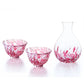 Set of three red and white glass sake cups and a carafe on a white background