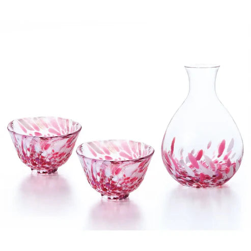 Set of three red and white glass sake cups and a carafe on a white background