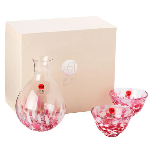 A colorful, speckled red and white sake glass set, includes one carafe and two cups, pictured in front of pink box packaging on a white background