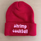 Red beanie with 'shrimp cocktail' text on a beige background