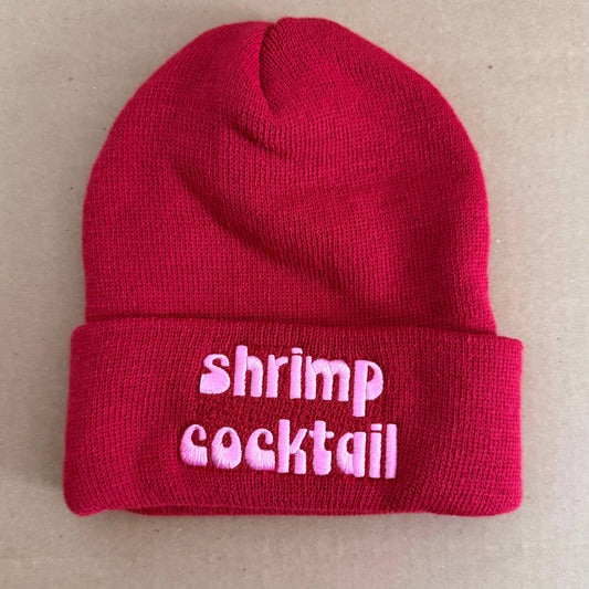 Red beanie with 'shrimp cocktail' text on a beige background