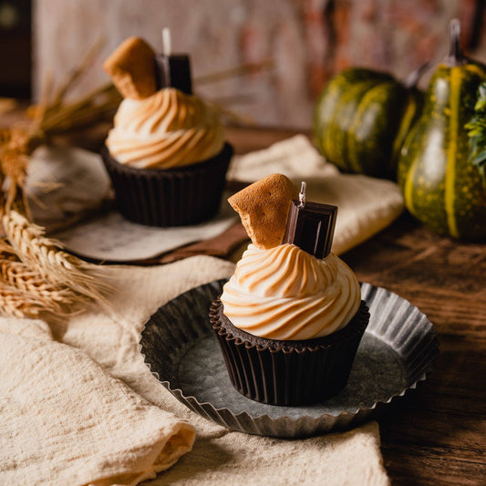 Realistic Smores Candle with chocolate cupcake base, whipped marshmallow topping and topped with a piece of chocolate and piece of graham cracker. Table set up with autumn fare. Two smores candles on the table.