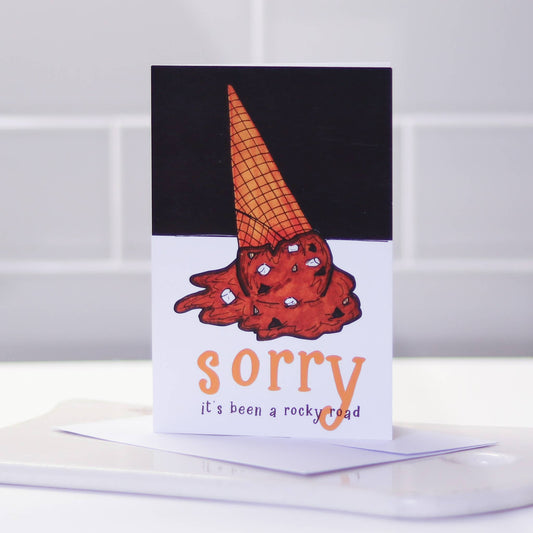 Greeting card with a melted rocky road ice cream cone upside down and text that reads "sorry it's been a rocky road" 