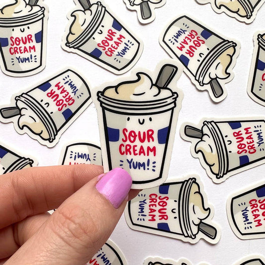 A hand with pink nail polish holds a die-cut sticker of a sour cream tub, surrounded by multiple identical stickers on a white background