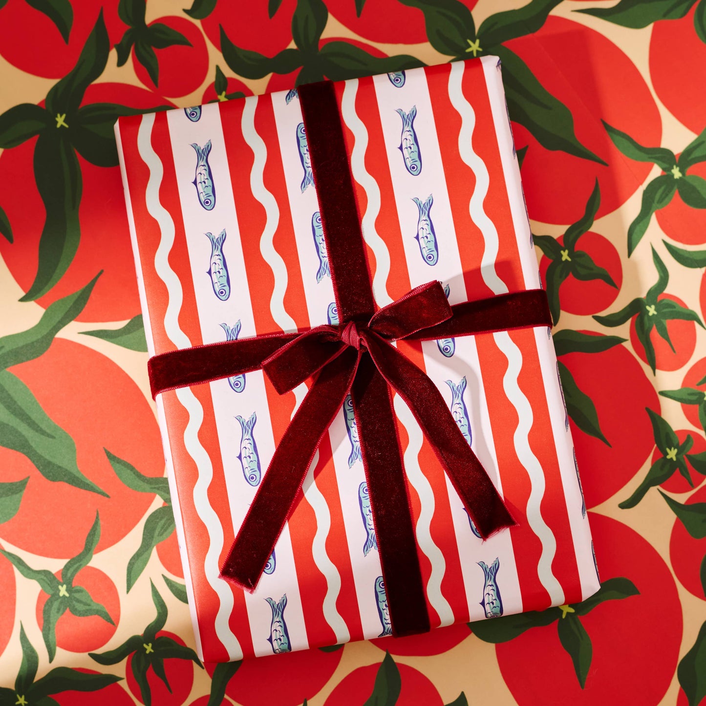 Gift wrapped in red and white striped paper with blue fishes with a brown ribbon on a festive background.