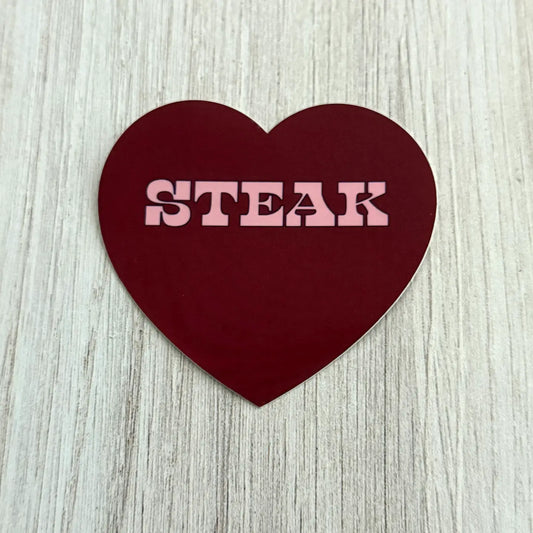 Heart-shaped sign with 'STEAK' text on a wooden surface