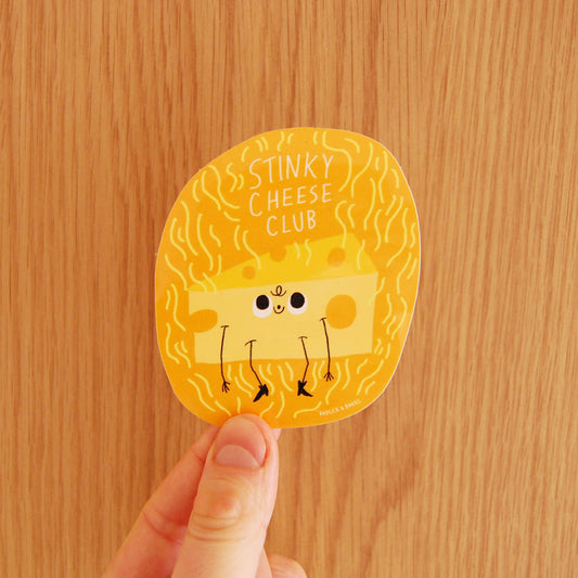 Round sticker with cartoon cheese character and 'Stinky Cheese Club' text held against a wooden background