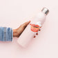 Person holding a pink water bottle with a decorative sticker on a light pink background