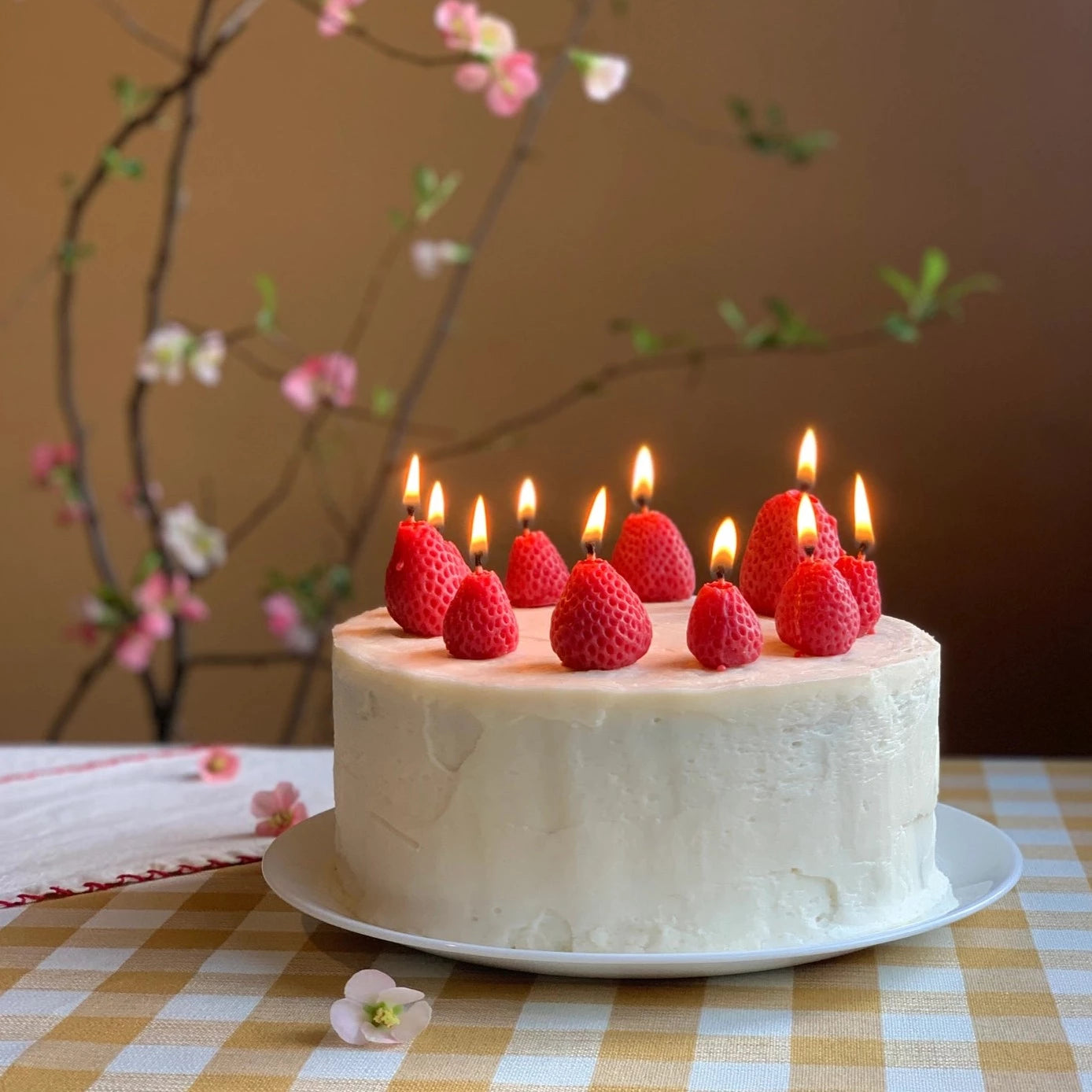 Realistic beeswax strawberry candles lit on a cake.