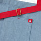 Blue apron with red straps. This apron is dedicated to strawberries with embroidery of strawberries in a basket and on a vine with little white flowers. Close up detail of red ampersand logo.
