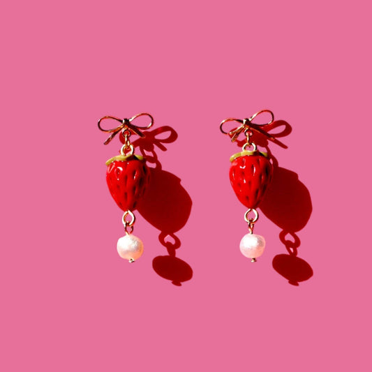 Strawberry-shaped earrings with pearl drops on a pink background