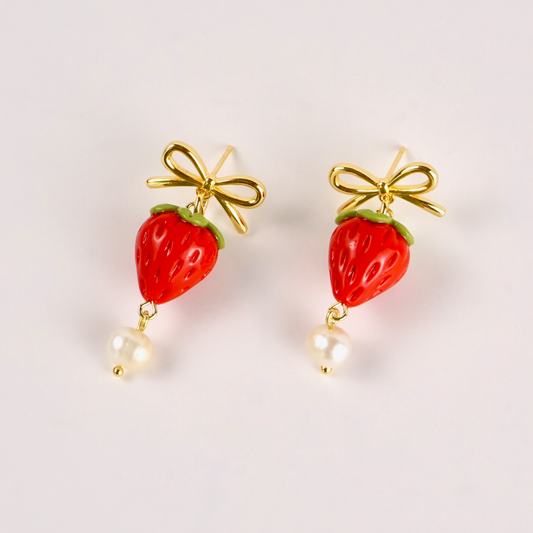 Strawberry-shaped earrings with gold bows and pearl drops on a light background